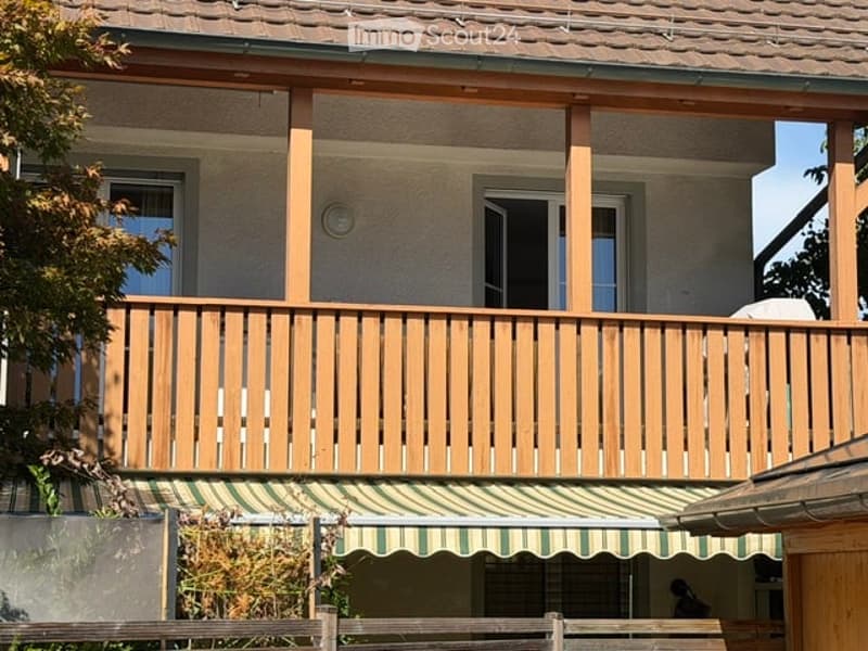 Two-story house with a wooden balcony and green striped awning. The balcony has wooden railings and is accessible from a window on the upper floor.