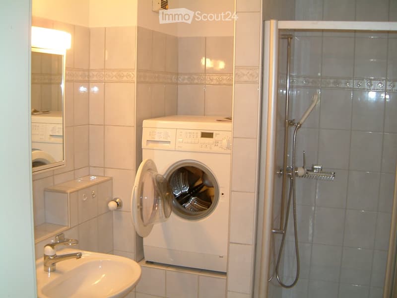 Bathroom with a sink, mirror, washing machine, and a shower stall.
