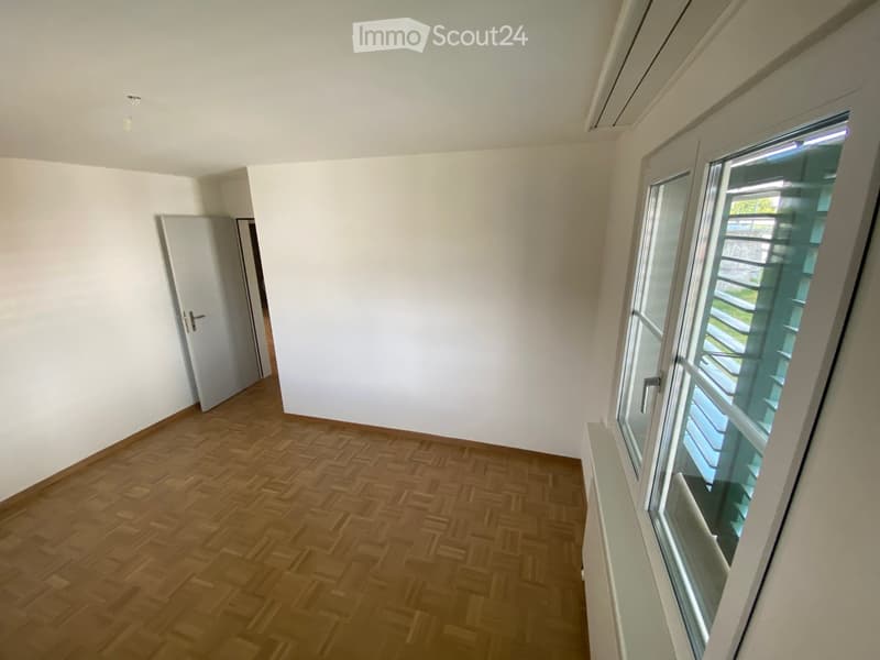 Empty room with wooden flooring, white walls, and a large window with a view of a balcony area.