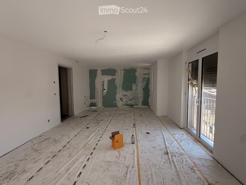 Empty room with bare walls, unfinished floor, and a partially open doorway. A small orange box and a bottle are on the floor.