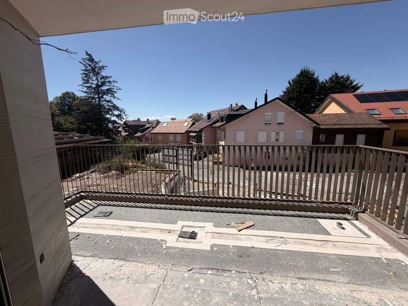 Balcony with metal railing, concrete floor, and a view of neighboring houses and trees.