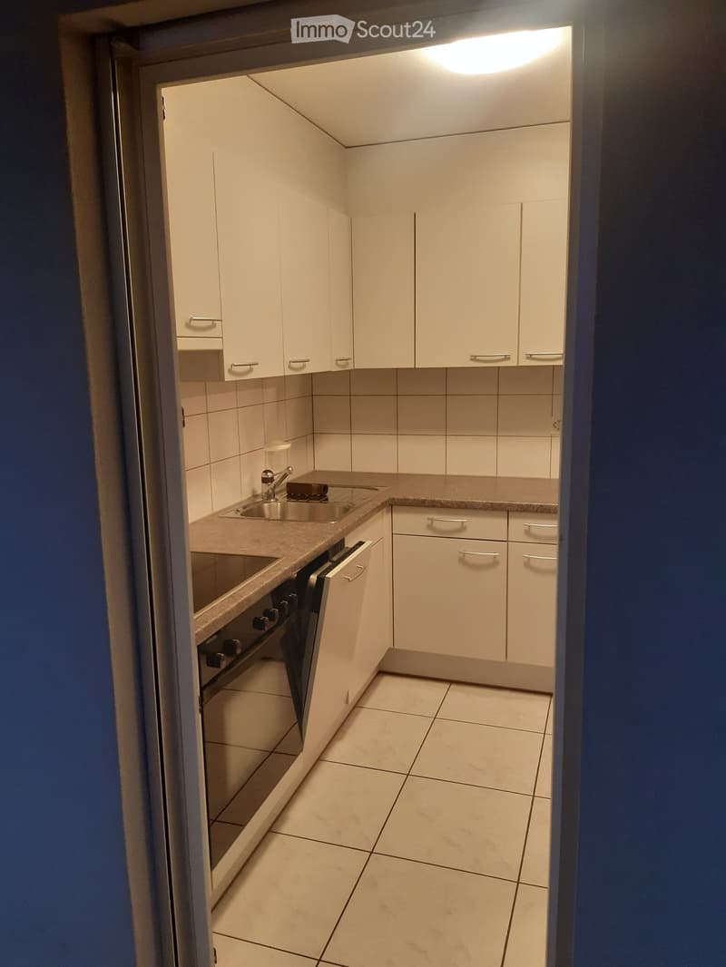 Compact kitchen with white cabinets, tiled walls, and a countertop with a sink and oven.