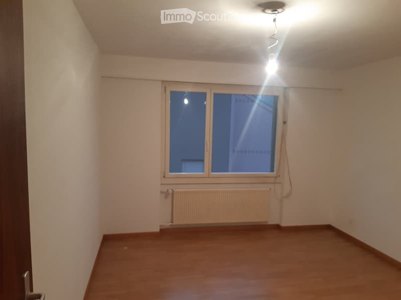 Empty room with wooden flooring, white walls, a window with double panes, and a radiator below the window.