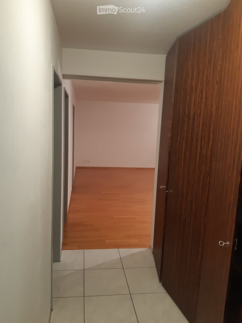 Empty hallway with wooden doors, tiled floor, and wooden flooring visible in the adjacent room.