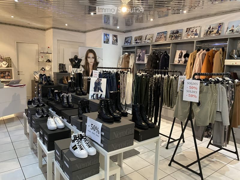 A well-lit clothing store with racks of coats and pants, shelves of shoes, and a mannequin displaying accessories.