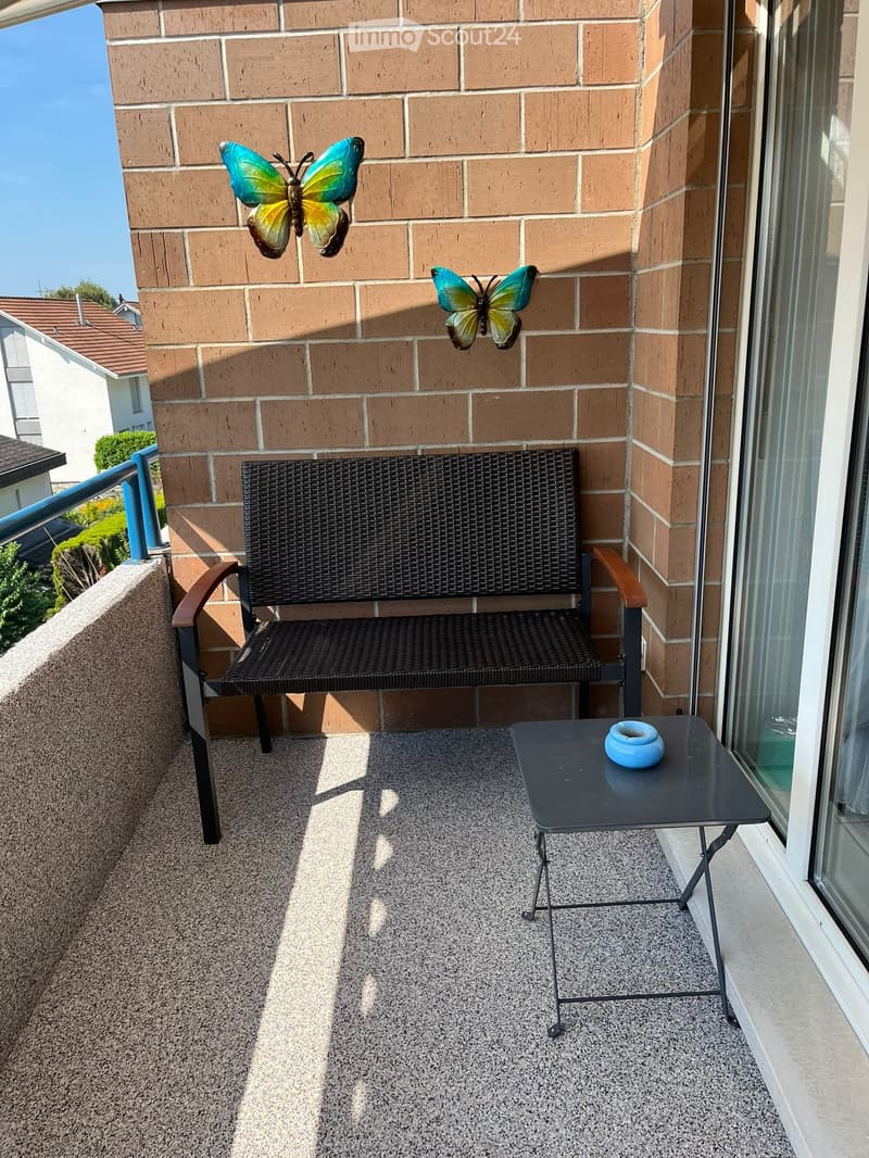 Balcony with a black wicker bench, small black table with a blue bowl, and two decorative butterflies on the wall.