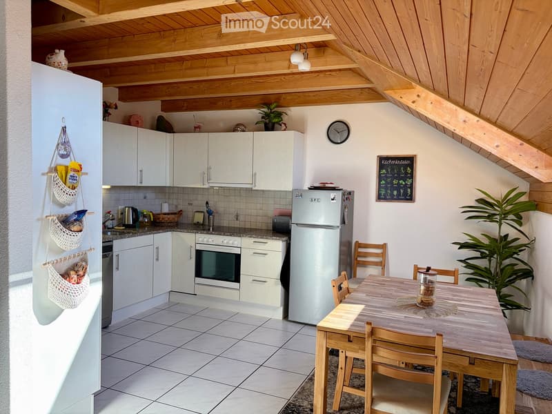 Bright kitchen with white cabinets, a wooden dining table with chairs, a refrigerator, and a clock on the wall.
