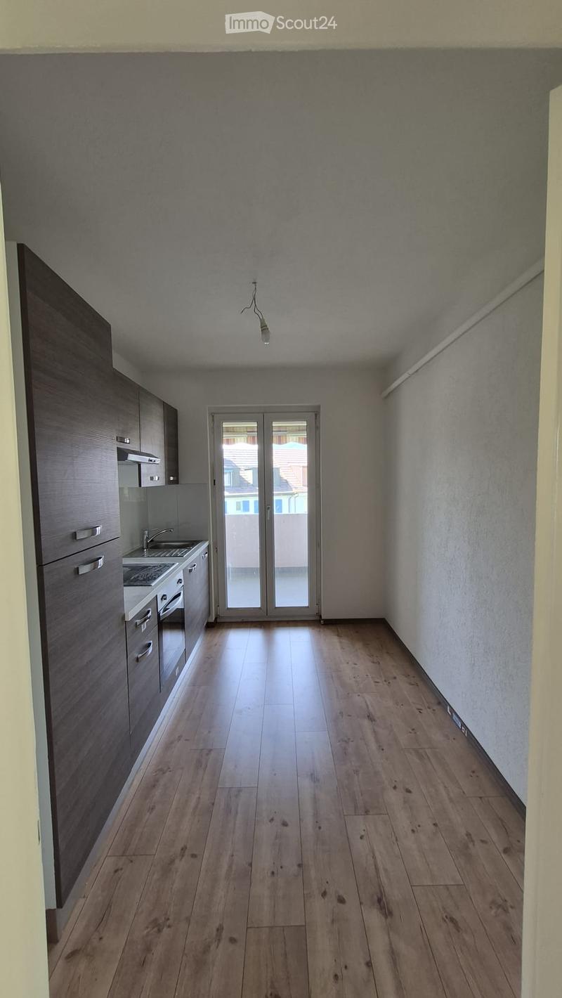 Modern kitchen with wooden flooring, grey cabinets, and a sink with a faucet. The space features a sliding glass door leading to a balcony.