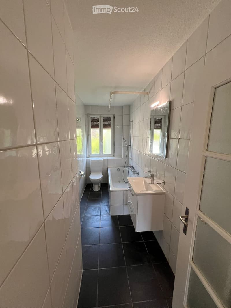 Modern bathroom with white tiles, black tiled floor, toilet, bathtub, sink, and mirror.