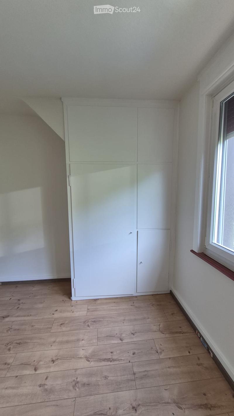 Empty room with wooden flooring, white walls, and a built-in white wardrobe with multiple doors.