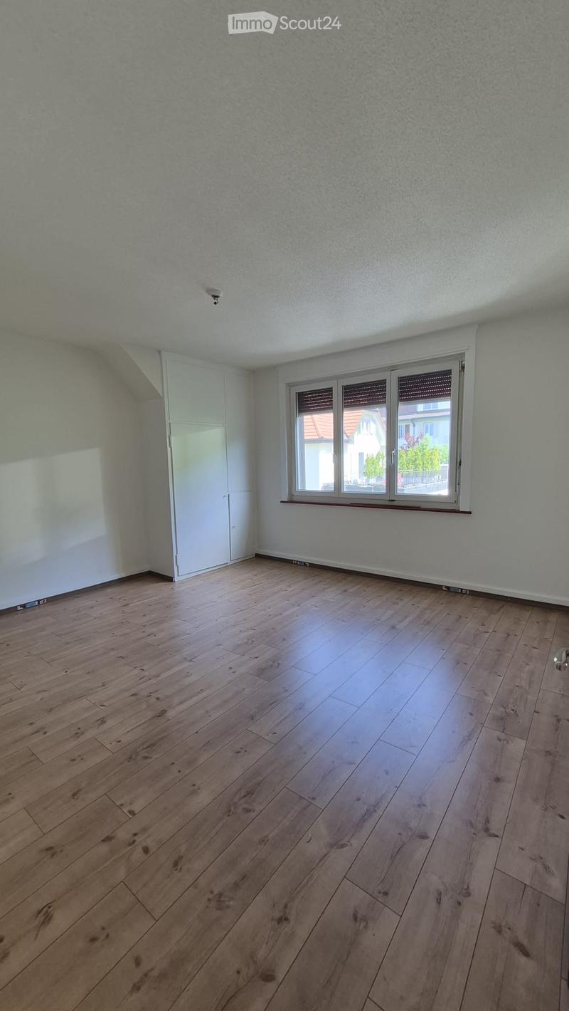Empty room with wooden flooring, white walls, and a large window with blinds. The room has a built-in closet on one side.