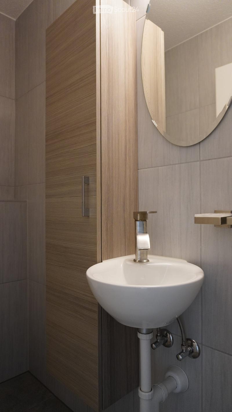 Modern bathroom with a white sink, chrome faucet, round mirror, and wooden cabinet.