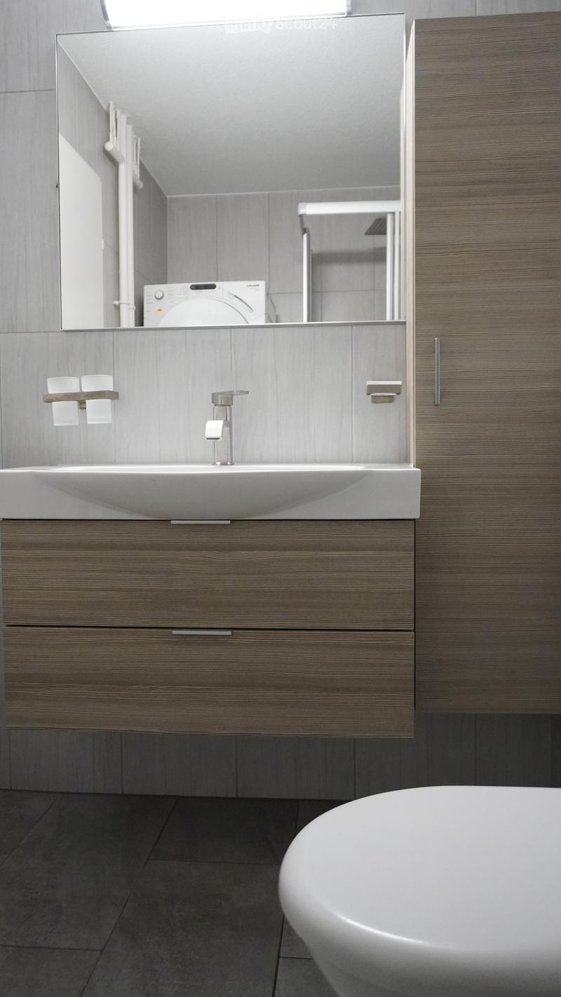 Modern bathroom with a sleek sink, faucet, mirror, and a bathtub. The vanity features wooden cabinets and drawers.