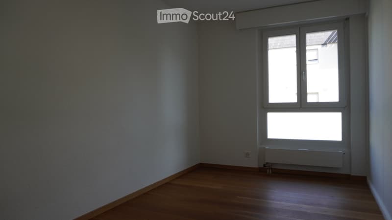 Empty room with wooden flooring, white walls, and a large window with double panes. A radiator is visible below the window.