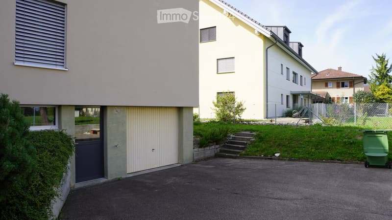 Modern two-story house with a raised ground floor, beige exterior, and a small garden area with steps leading up to the entrance.