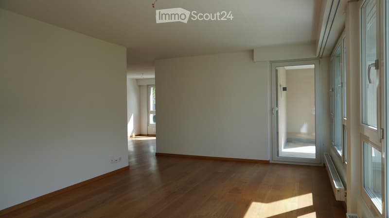 Empty room with wooden flooring, white walls, and large windows allowing natural light. No furniture or equipment present.