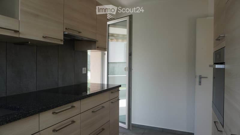 Modern kitchen with light wooden cabinets, granite countertop, and stainless steel appliances. Features an open sliding door leading to a balcony.