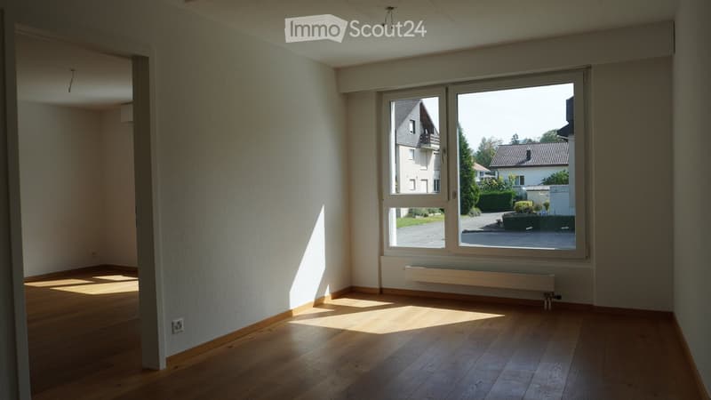 Empty room with wooden flooring, large window, radiator, and natural light. No furniture or equipment present.
