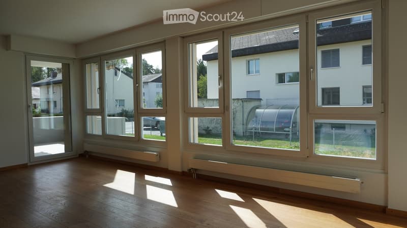 Empty room with wooden flooring, large windows, radiators, and a sliding door leading to an outdoor area.