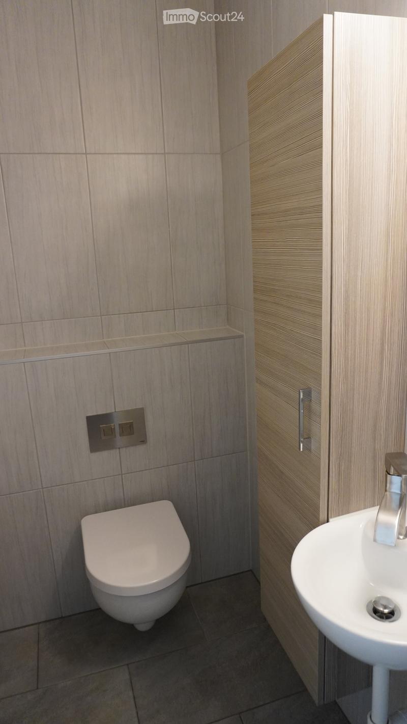 Modern bathroom with a toilet, sink, and sleek wooden cabinetry. Light-colored tiles and a dark floor complete the design.