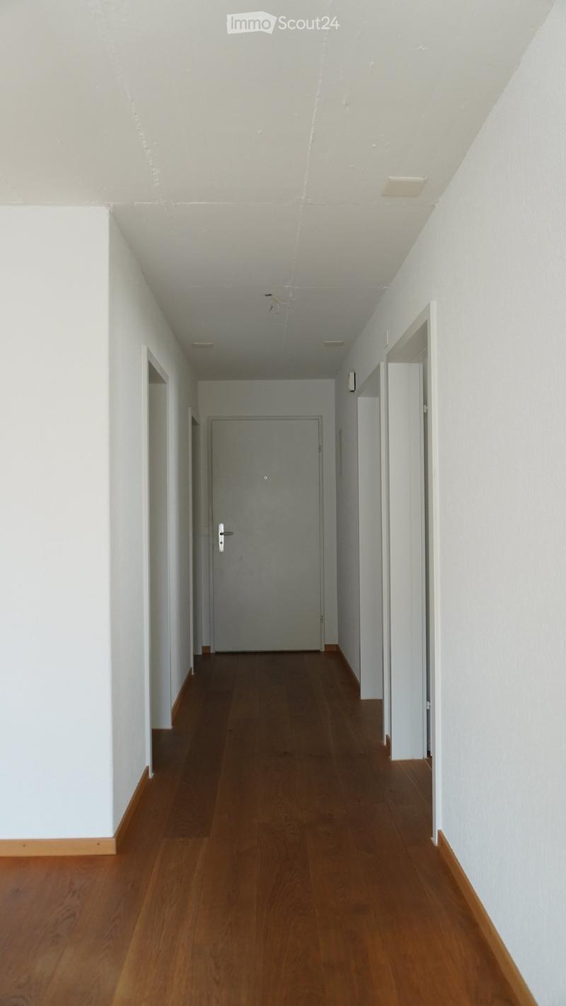 Empty hallway with wooden flooring, white walls, and a closed door at the end.