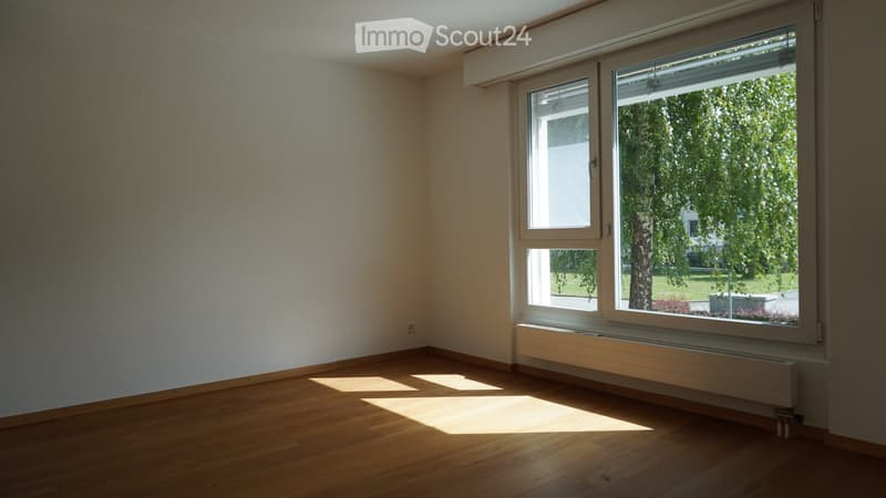 Empty room with wooden flooring, white walls, and large windows letting in natural light. No furniture or equipment present.