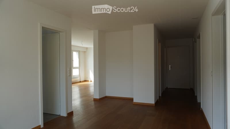 Empty hallway with wooden flooring, white walls, and doors leading to other rooms.