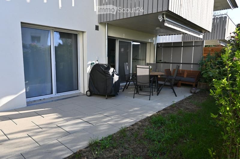Balcony area with tiled floor, covered grill, outdoor dining set, bench, and greenery.