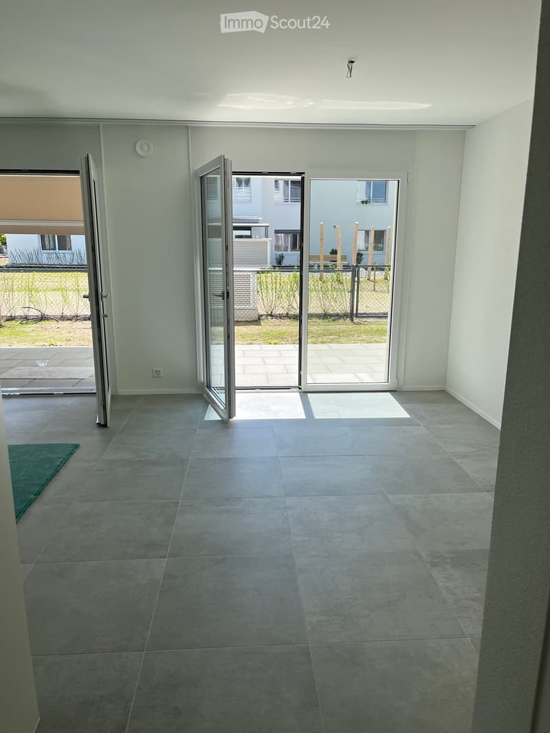 Empty room with grey tiled floor, white walls, and large sliding glass doors leading to a patio area.