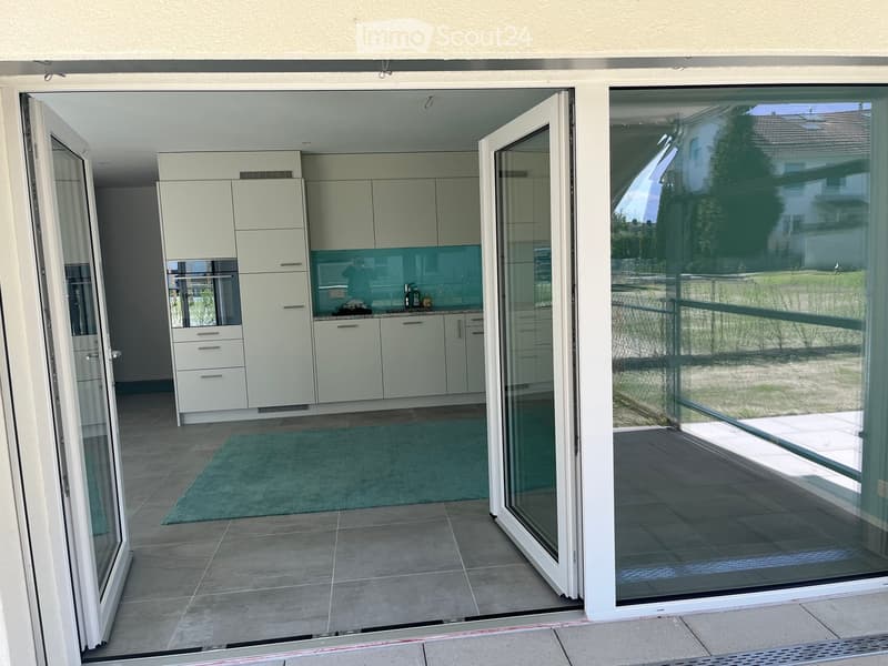 Modern kitchen with white cabinets, a sink, and a bottle on the counter, connected to a tiled patio through large glass doors.