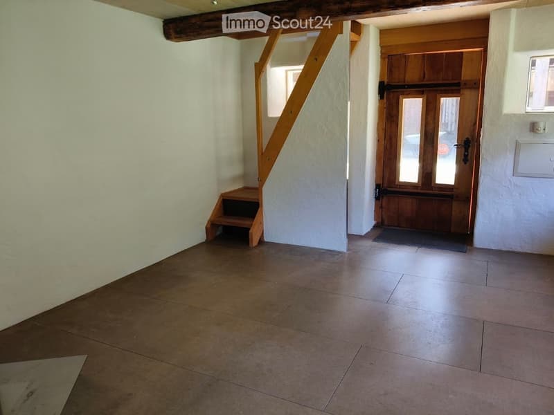 Empty hallway with tiled floor, white walls, wooden staircase, and a wooden door leading outside.