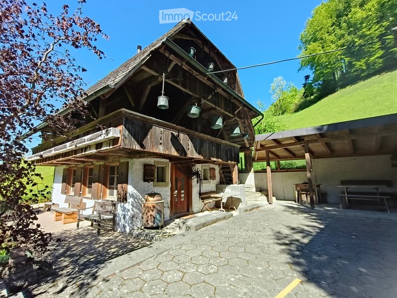 Traditional wooden house with a raised ground floor, featuring a balcony, wooden benches, and outdoor seating area.