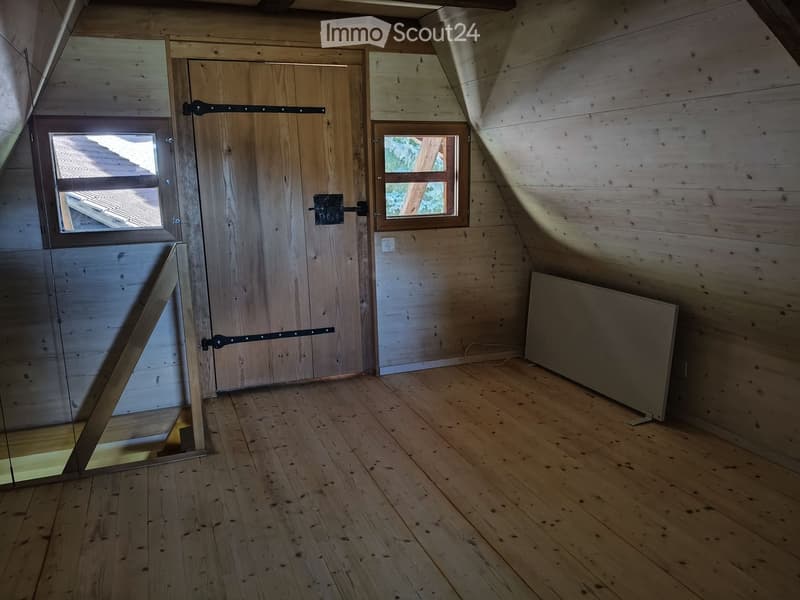 Empty attic room with wooden walls, wooden floor, and a large wooden door with windows on either side.