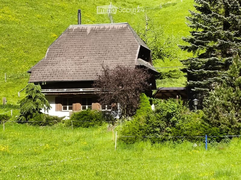 A two-story house with a sloped roof, surrounded by lush green grass and trees.