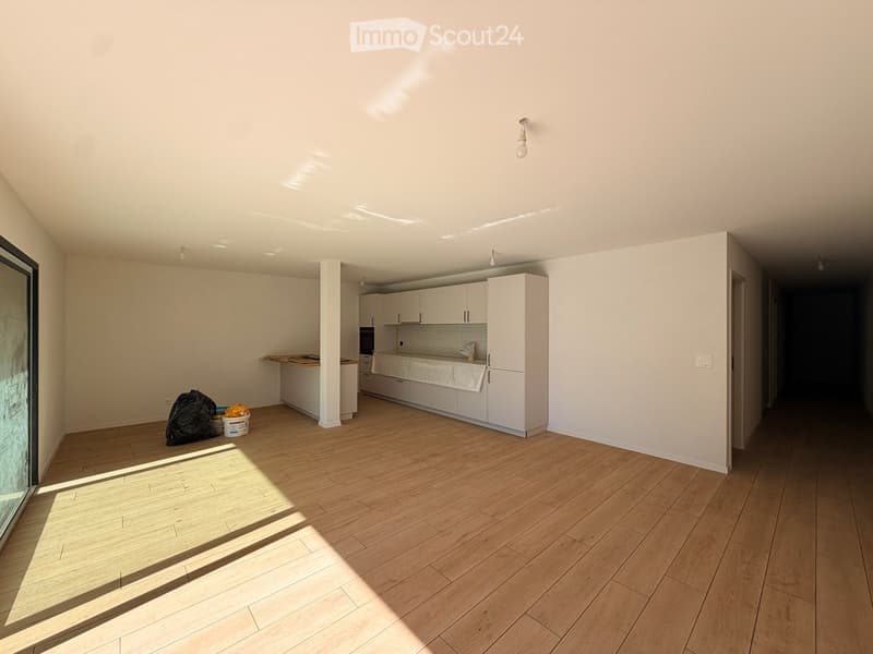 Bright, modern kitchen with white cabinets, wooden flooring, and natural light from a large window. Includes an oven and refrigerator.