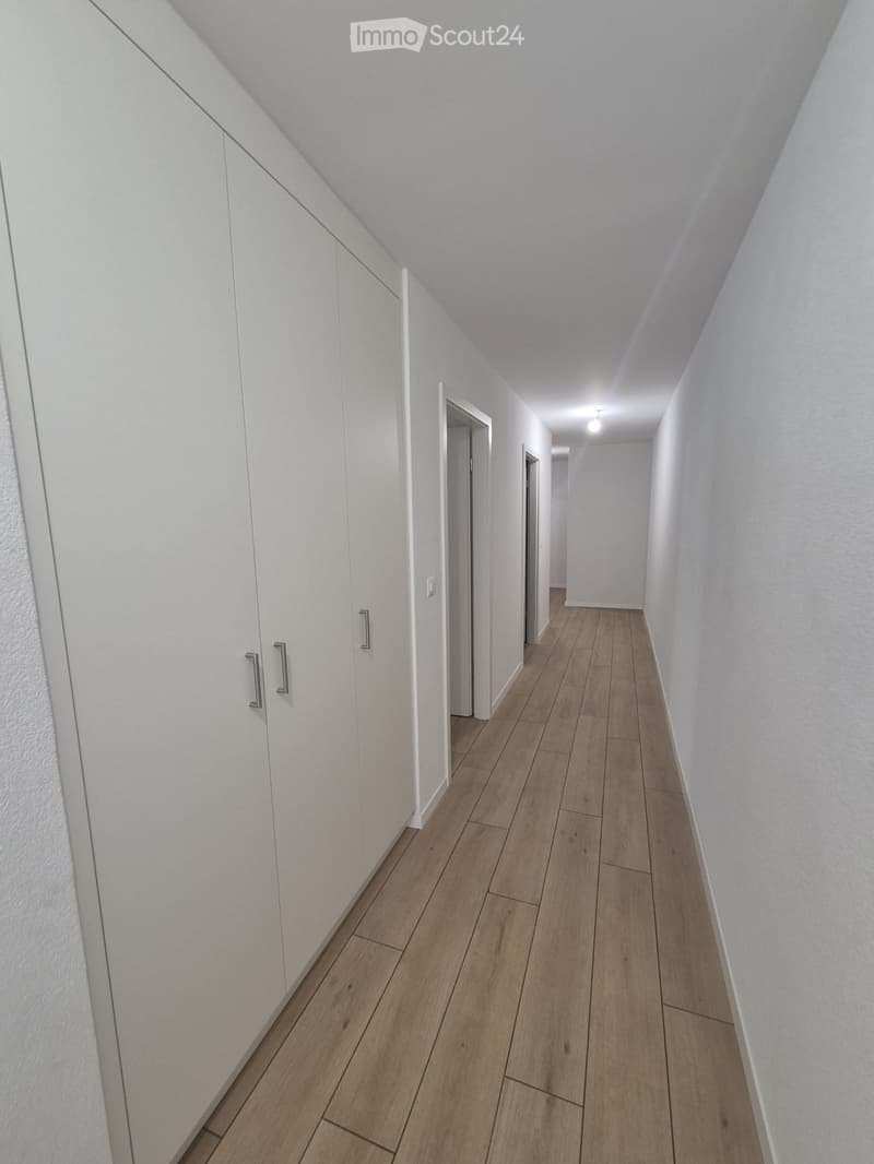 Empty hallway with light wooden flooring, white walls, and built-in white cabinets on one side.