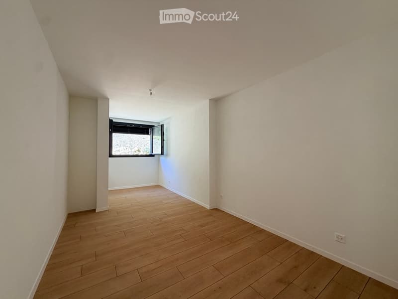 Empty room with light wooden flooring, white walls, and a single window with black frame. No furniture or equipment present.
