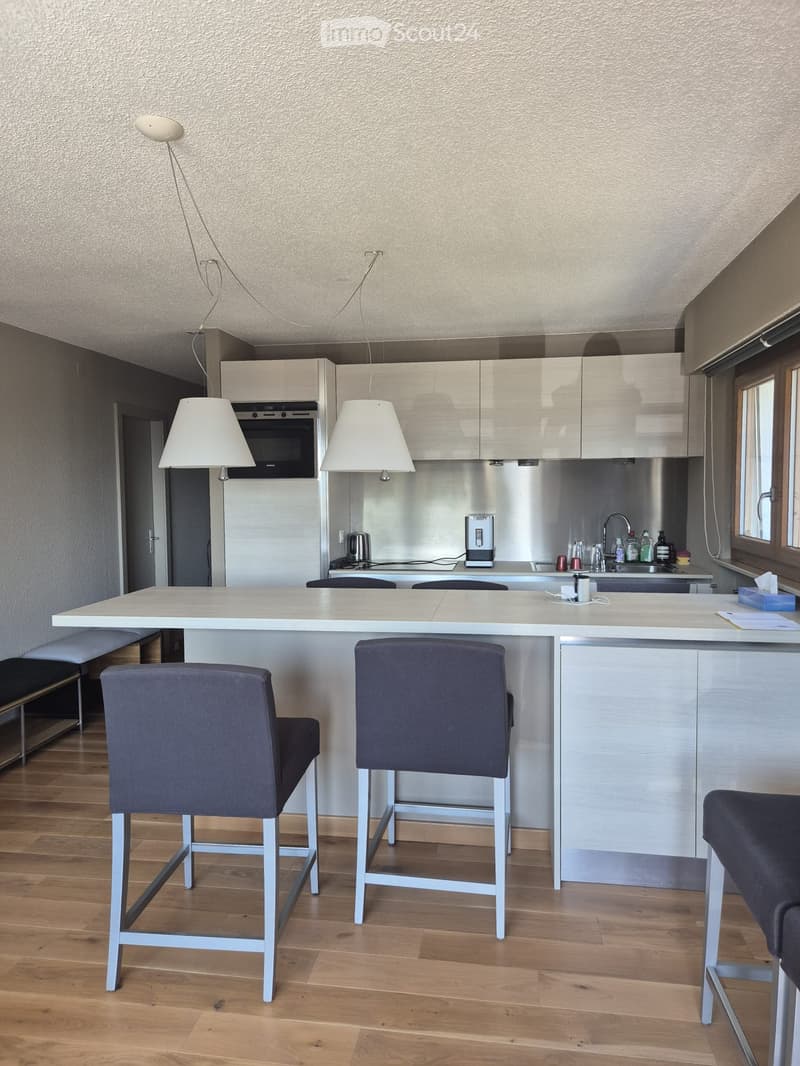 Modern kitchen with white cabinets, stainless steel appliances, a central island with bar stools, and pendant lighting.