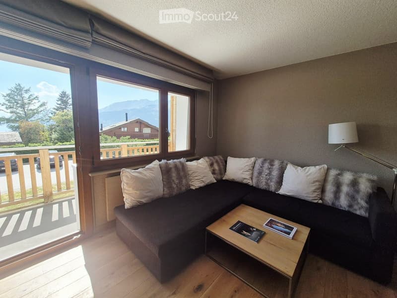 Modern living room with a dark sectional sofa, wooden coffee table, and large windows offering a scenic mountain view.
