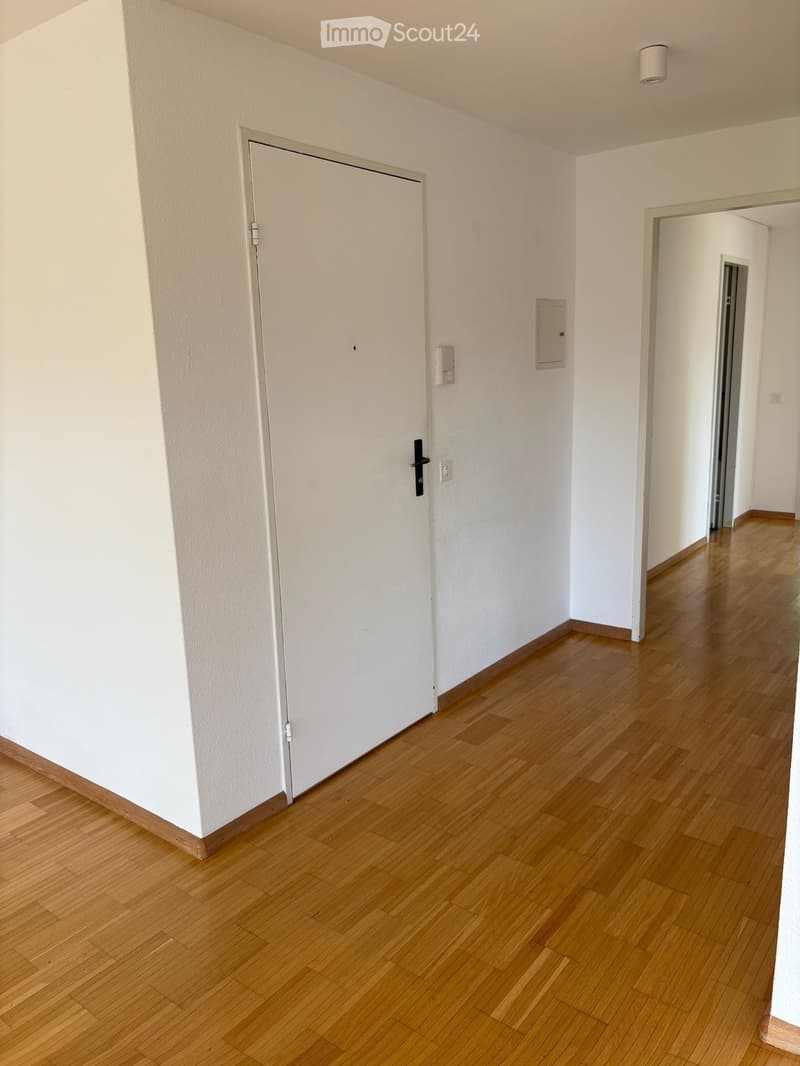 Empty hallway with wooden flooring, white walls, and a closed door on the left side.
