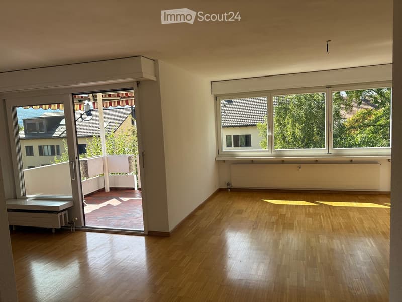 Empty room with wooden flooring, large windows, and a sliding glass door leading to a balcony area.