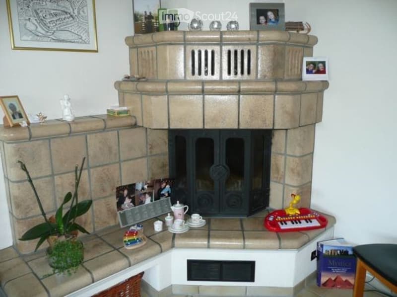 A cozy fireplace area with a decorative mantel, teapot, cups, picture frames, and a small plant on the hearth.