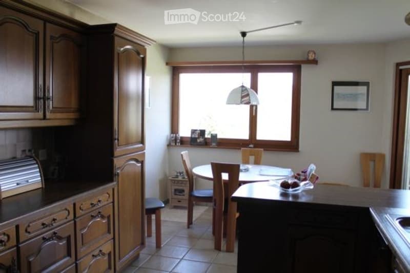 Bright kitchen with wooden cabinets, a dining area with a table and chairs, and a window letting in natural light.
