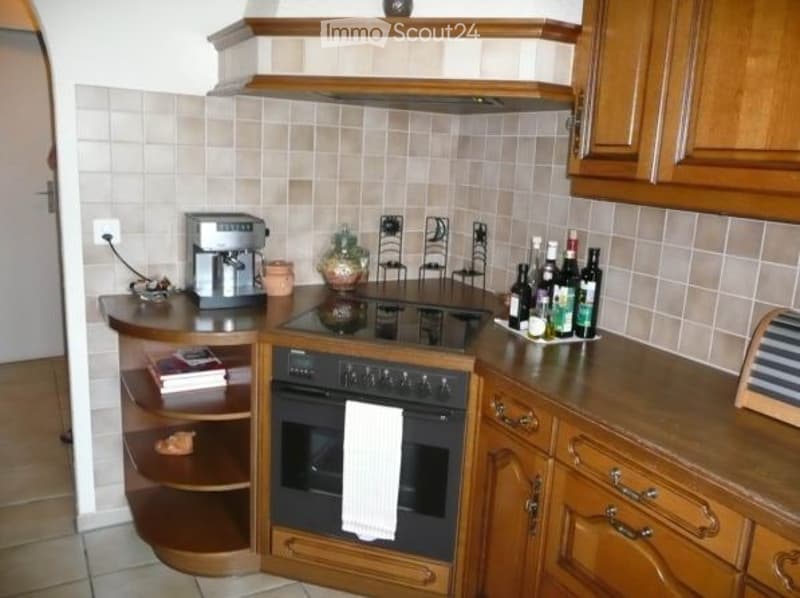 A cozy kitchen with wooden cabinets, a coffee maker, an oven, and various bottles and cups on the counter.