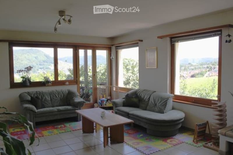 Bright living room with large windows offering a scenic mountain view, featuring two sofas, a coffee table, and a colorful play mat.
