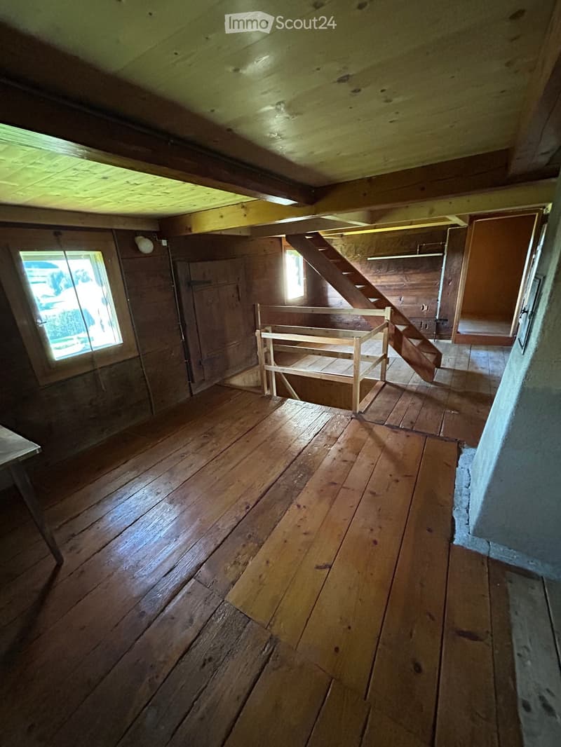 Empty attic space with wooden floors, exposed wooden beams, and a small wooden staircase leading upwards.