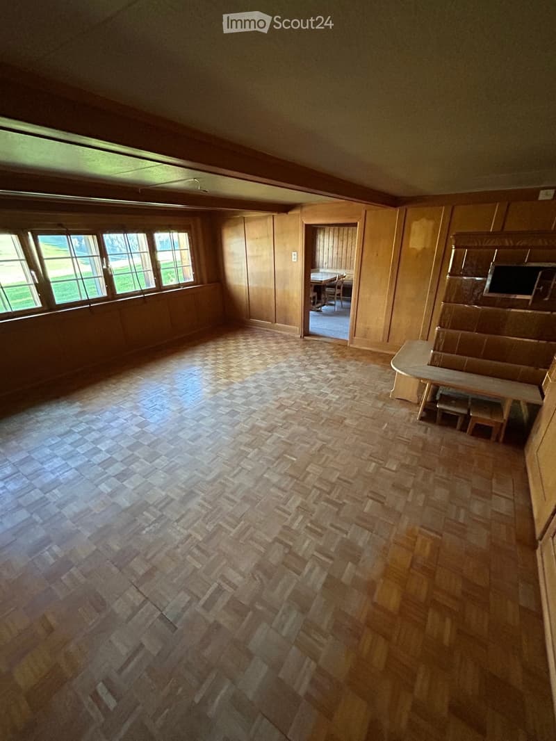 Empty room with wooden walls, herringbone-patterned tile floor, large windows, and a doorway leading to another room.