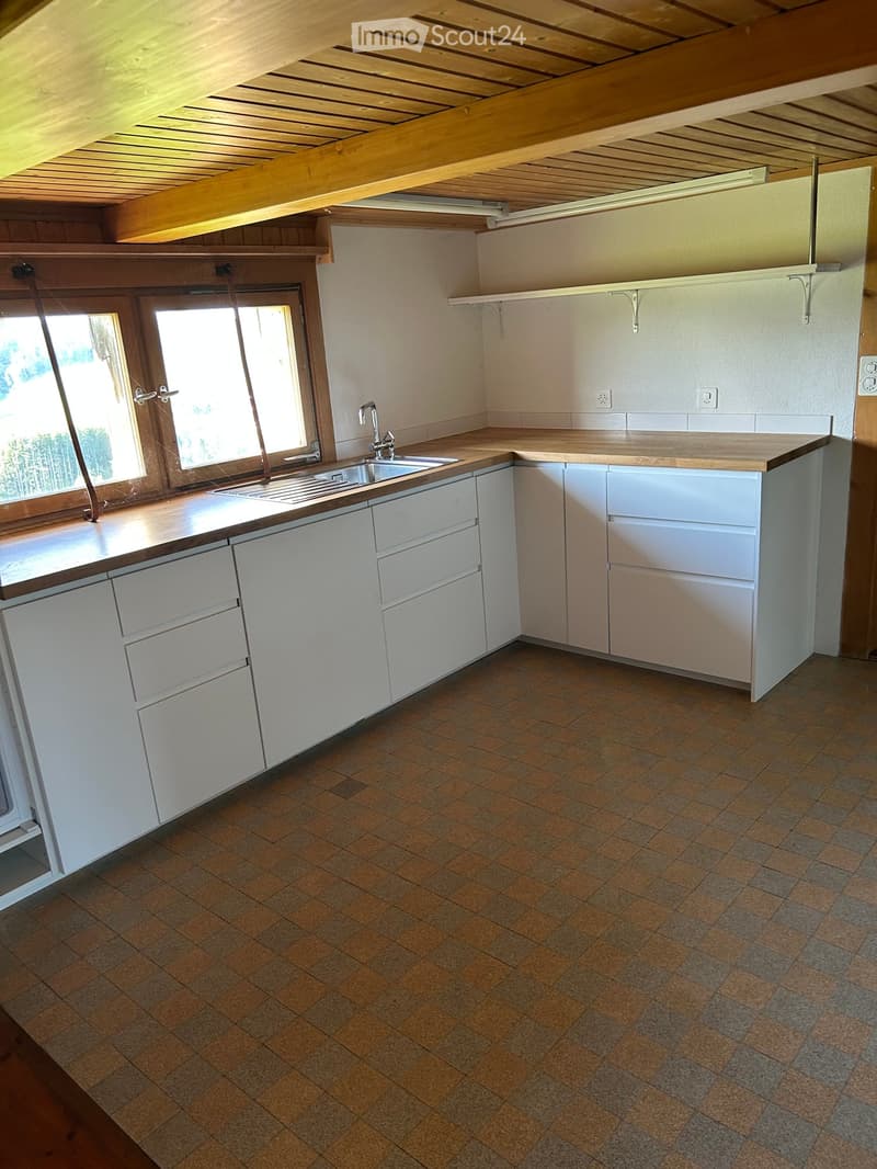 Bright kitchen with white cabinets, wooden countertop, and tiled floor. Features a sink with a faucet and a window with wooden frame.