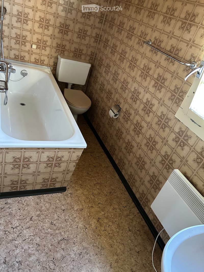 Bathroom with a bathtub, toilet, and tiled walls in a classic pattern. Includes a faucet and a visible roll of toilet paper.