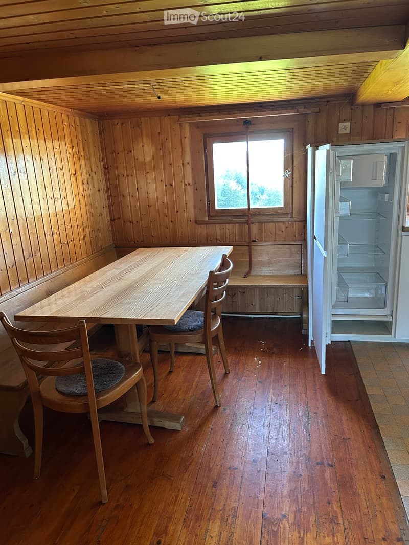Cozy wooden kitchen with a dining table, chairs, and an open refrigerator, featuring wooden walls and floors.